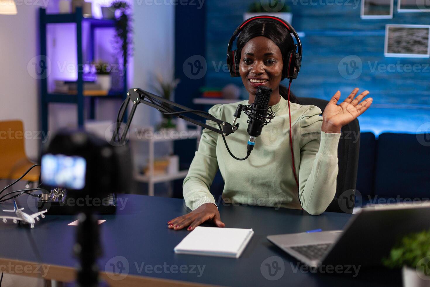 Social media woman creator greeting subscribers while recording content for youtube channel. Influencer sitting in podcast studio filming tutorial using production equipment. On air talk show photo