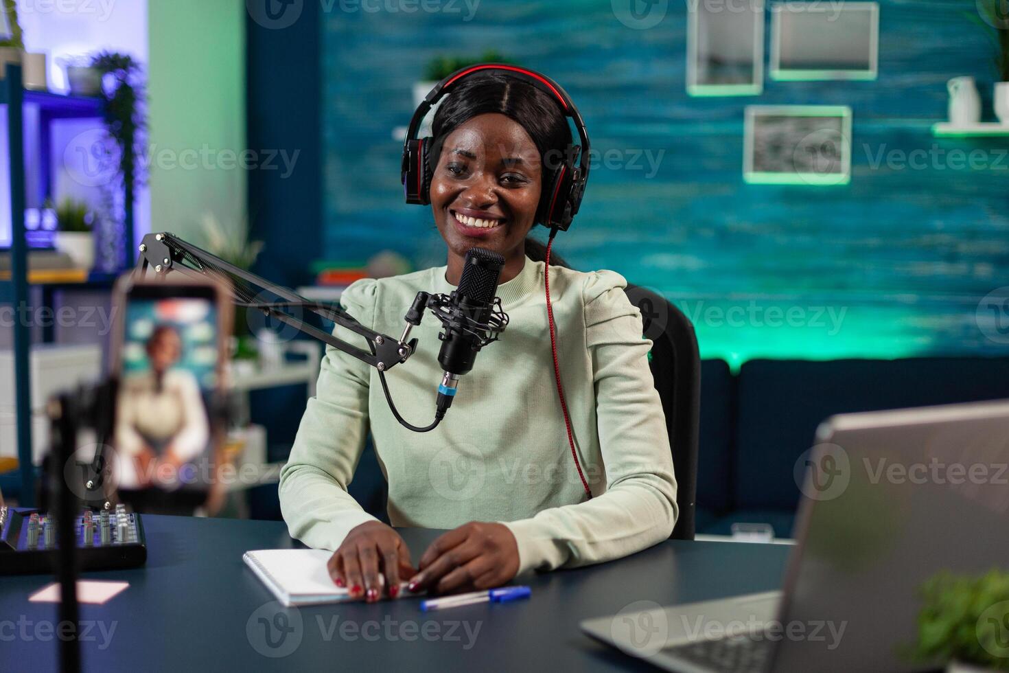 African american influencer woman smiling while recording content using modern smartphone for social media. Vlogger person talking with youtube answering subscribers questions photo