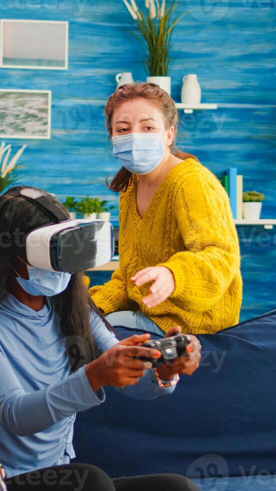 Mixed group of people guiding black woman with vr headset playing virtual games in living room keeping social distancing agaist covid19. Diverse friends having fun at new normal party. photo