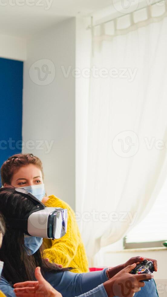 Black woman experiencing virtual reality headset playing games wearing face mask while friends having fun drinking beer. respecting distancing wearing face mask to prevent infection with virus, photo