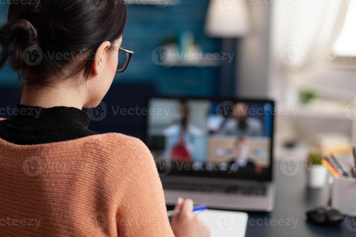 Student in group videocall taking notes. Over the shoulder view of freelancer having briefing call with team in home office and discussing with colleagues in webcam conference. photo