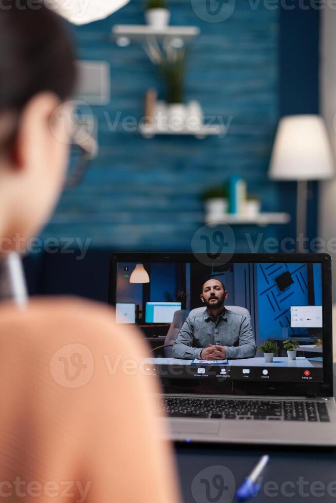 Freelancer with laptop in a videocall with client. Over the shoulder view of student attending online lesson with teacher from home. Man talking in online webinar conference. photo