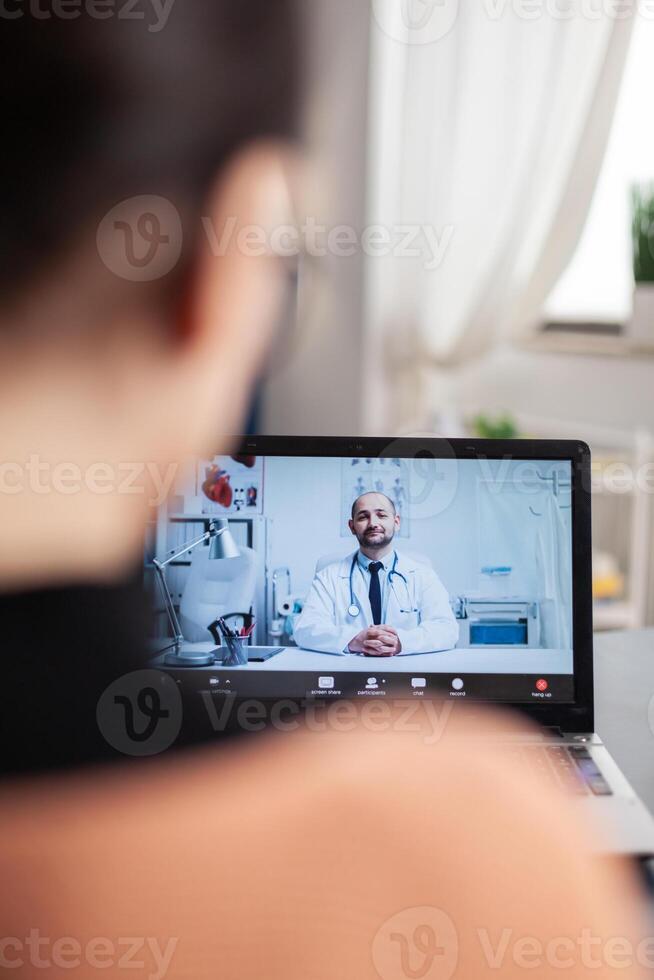 Student working from home videocalling doctor on laptop. Over shoulder view of freelancer in online medical consultation call. Physician gives health advice on webcam. photo