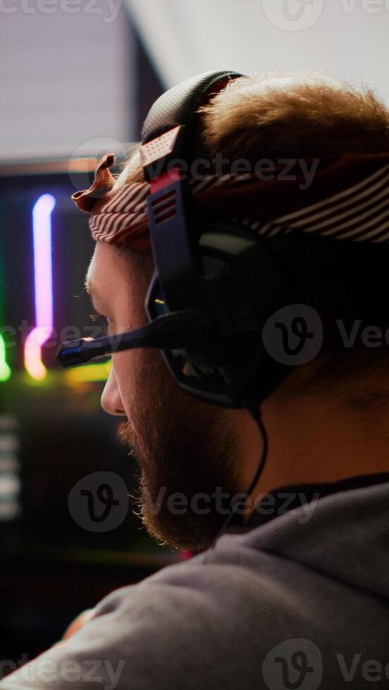 Focused man gamer putting headset playing shooter online game on RGB powerful computer in living room late night. Pro cyber streaming gaming championship, participating in eSports tournament photo