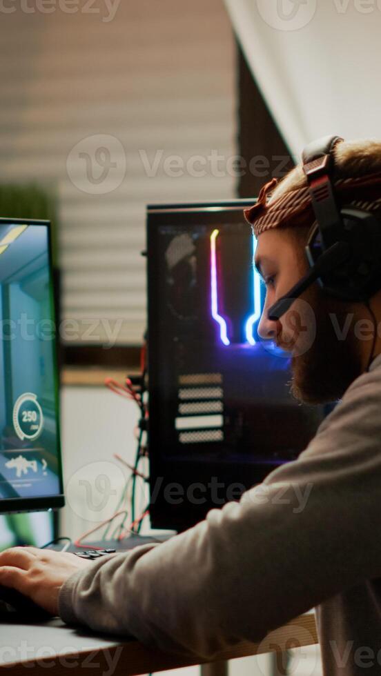 Cyber sport gamer wearing headphones playing first person shooter videogame participating in eSports tournament perforing at RGB prowerful personal computer. Pro cyber streaming gaming championship photo