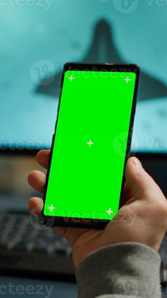 Competitive gamer looking at smartphone with green screen chroma key desktop playing online games on powerful computer during live tournament. Cyber player using phone with mock up isolated display photo