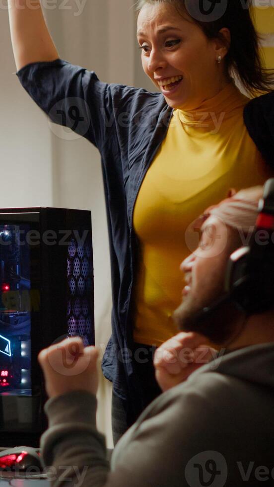 Excited couple gamer winning first person shooter online game on RGB powerful computer screaming raising hands. Pro cybers performing during gaming tournament esport championship wearing headset photo