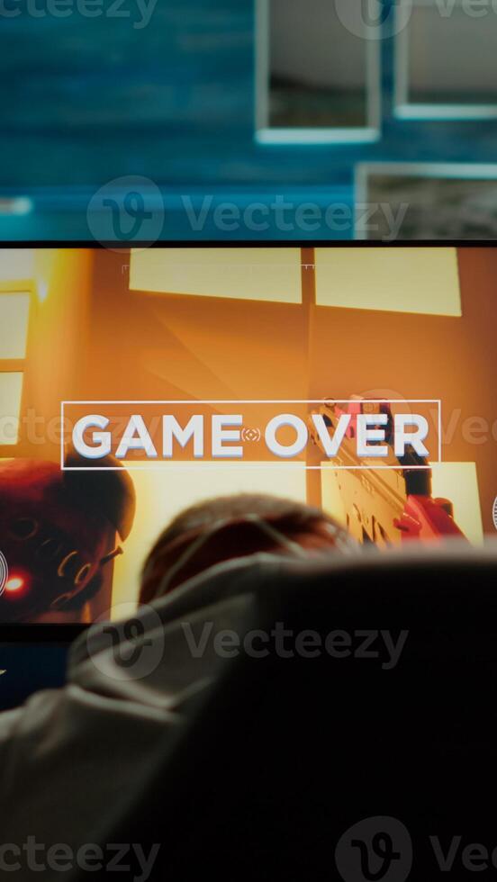 Back view of sad professional eSports gamer losing shooter mock-up game. Defeated man with headphones streaming online cyber performing during gaming tournament using powerful personal computer photo