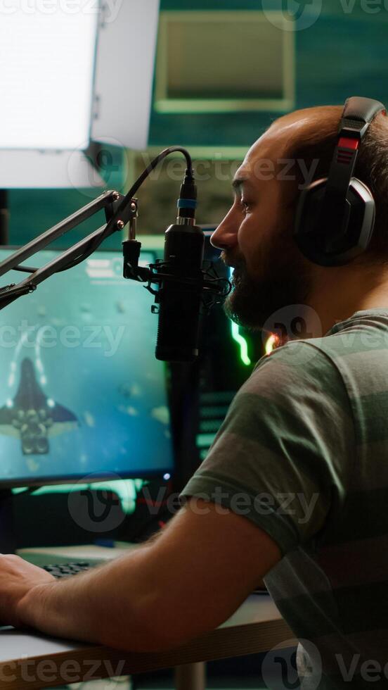 Pro cyber man streaming videogame, reading on stream chat and playing space shooter on RGB powerful computer. Streamer sitting on gaming chair playing game during online esports tournament. photo