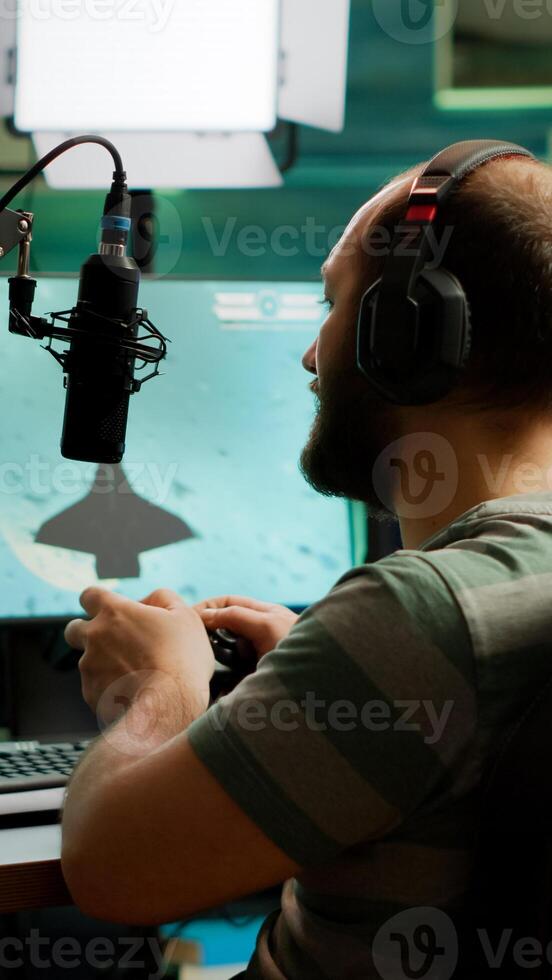 Man streamer playing space shooter games using professional RGB keyboard and wireless joystick. Pro gamer talking into microphone on streaming chat during online tournament photo