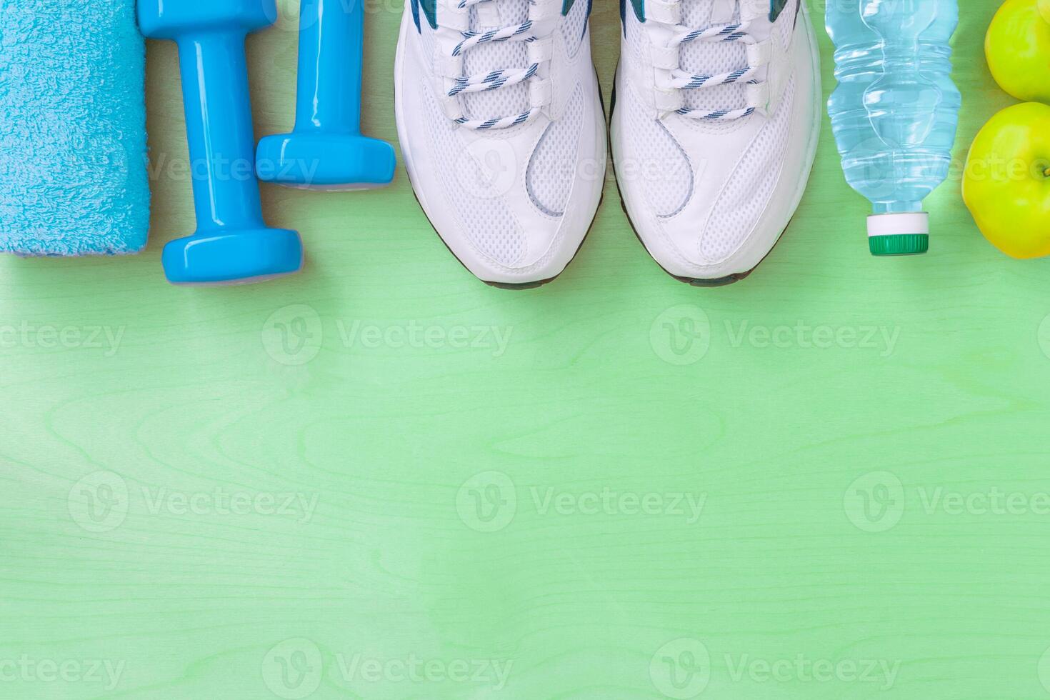 Attributes of a healthy lifestyle water, apples, sports equipment on bright green surface. Flat view with copy space. photo