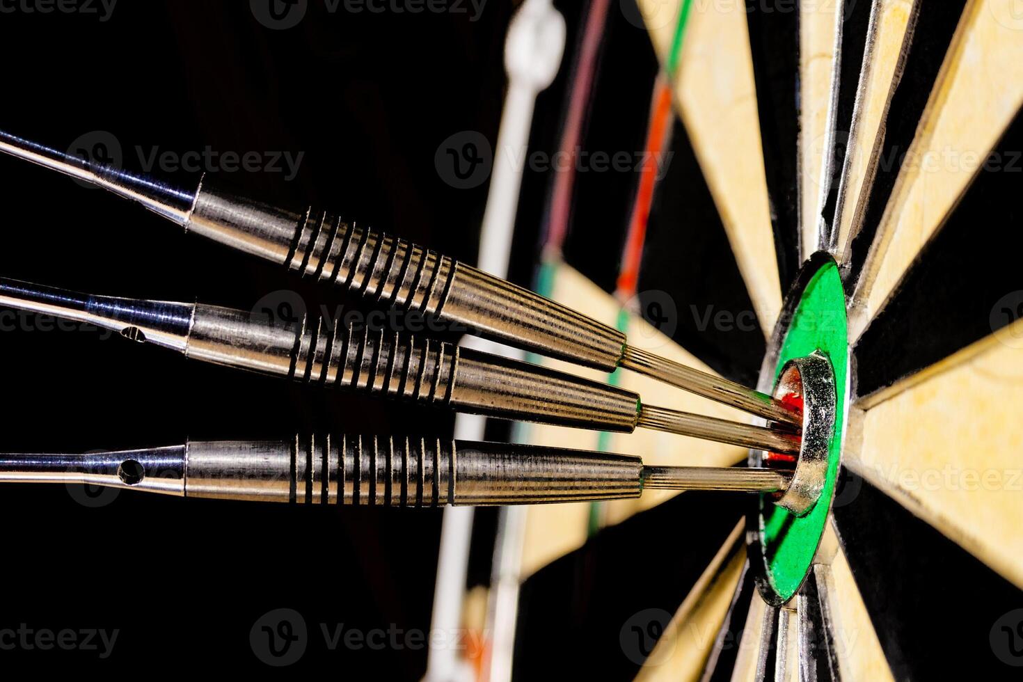Sisal dartboard with three darts in a bullseye on a black background photo