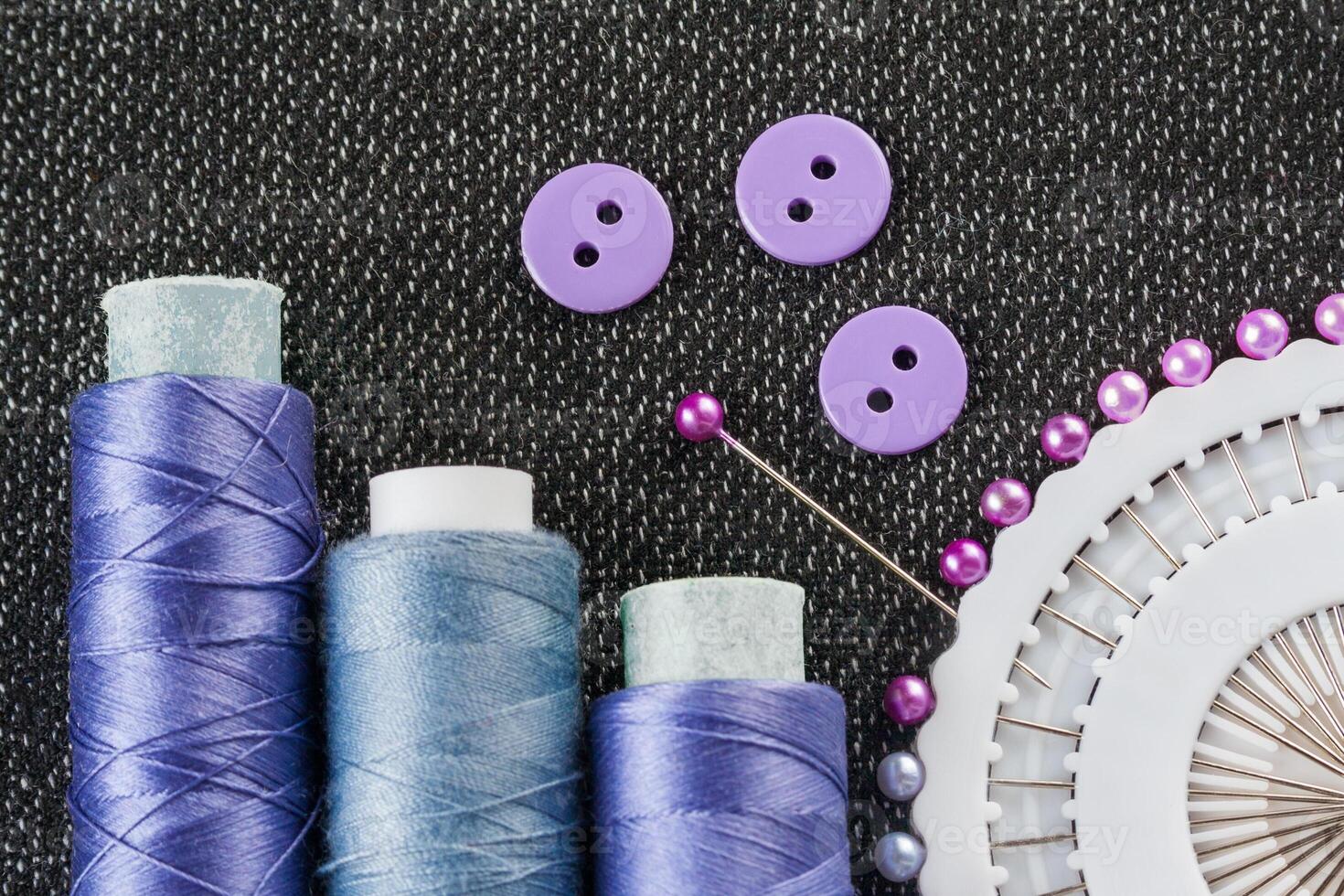 Sewing accessories spools of threads, needles, buttons, on the textured fabric surface photo