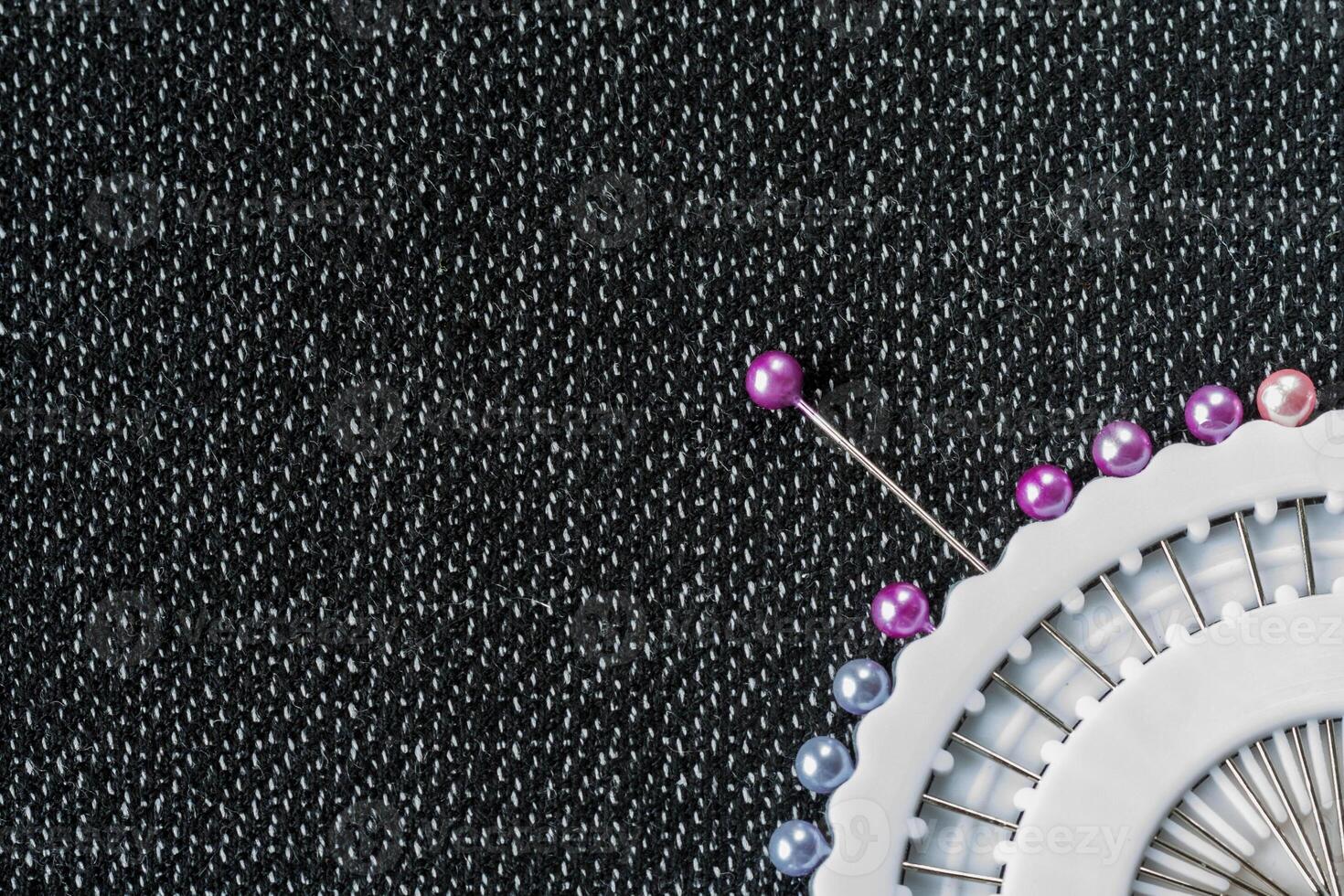 Fragment of a white sewing needles container on a dark textured fabric surface. Top or flat view with copy space photo
