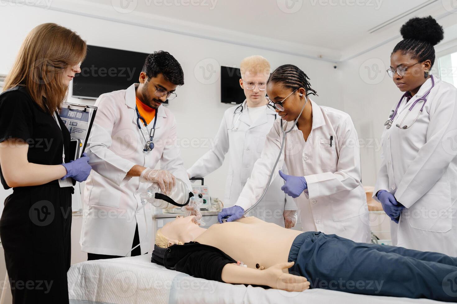 A group of five medical students stand around a training dummy, practicing CPR in a medical training facility photo