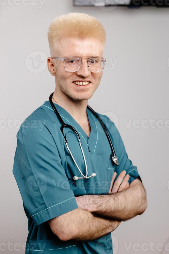 A male doctor in a teal scrub top and stethoscope smiles for the camera photo