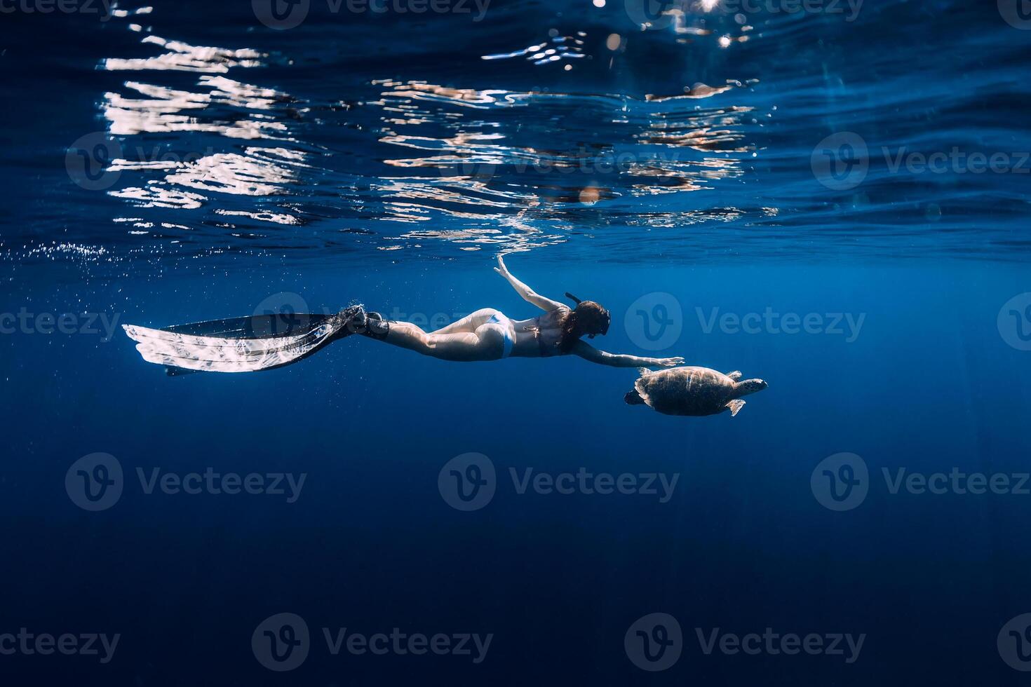 Woman freediver with fins glides underwater with sea turtle in tropical sea. Snorkeling with turtle in ocean. photo