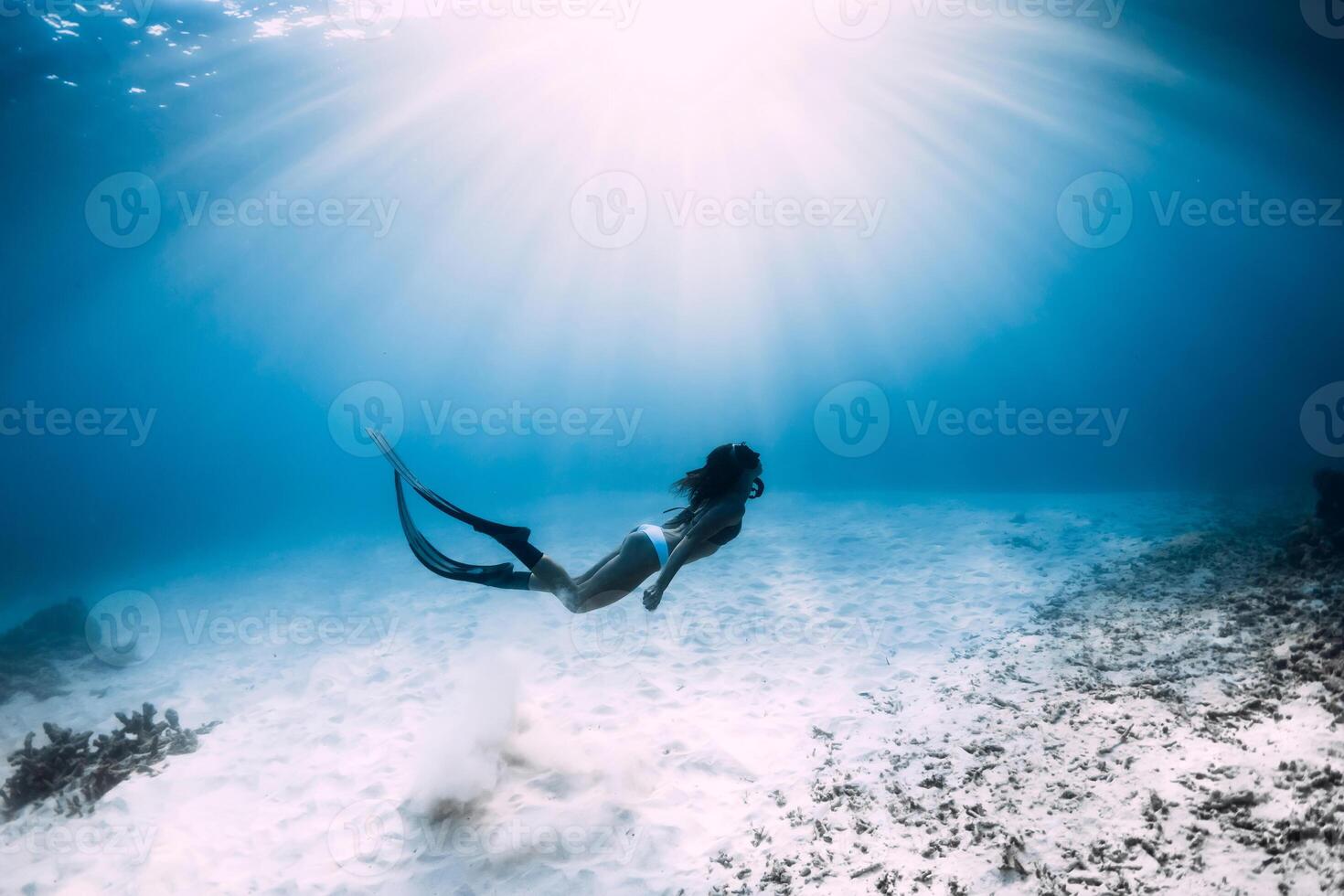 Free diver girl with fins glides over sandy sea in ocean. Freediver and amazing light photo