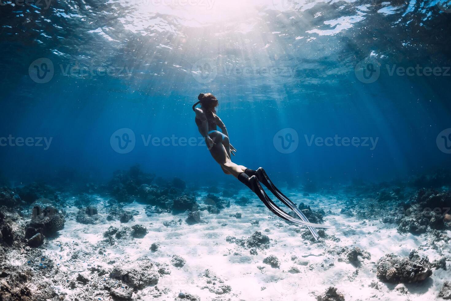Woman free diver with fins glides underwater in deep blue ocean photo
