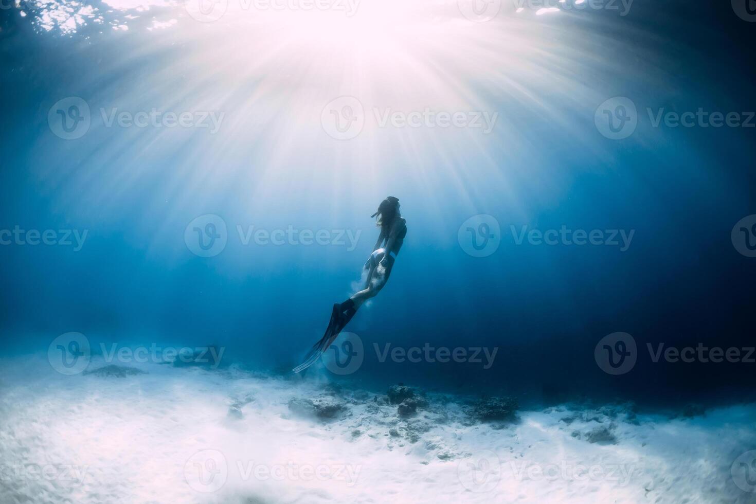 Freediver woman with fins glides over sandy sea bottom in sea. Freediver and amazing light photo