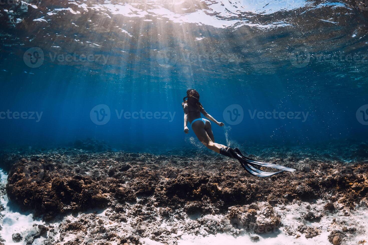 Woman freediver with fins glides underwater in blue ocean. Freediving or swimming in sea photo