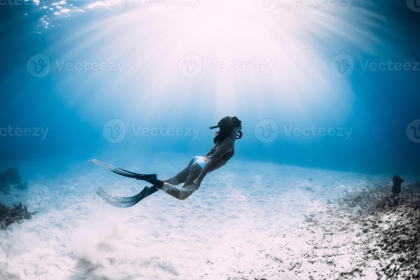 Freediver woman with fins dive over sandy sea in sea. photo