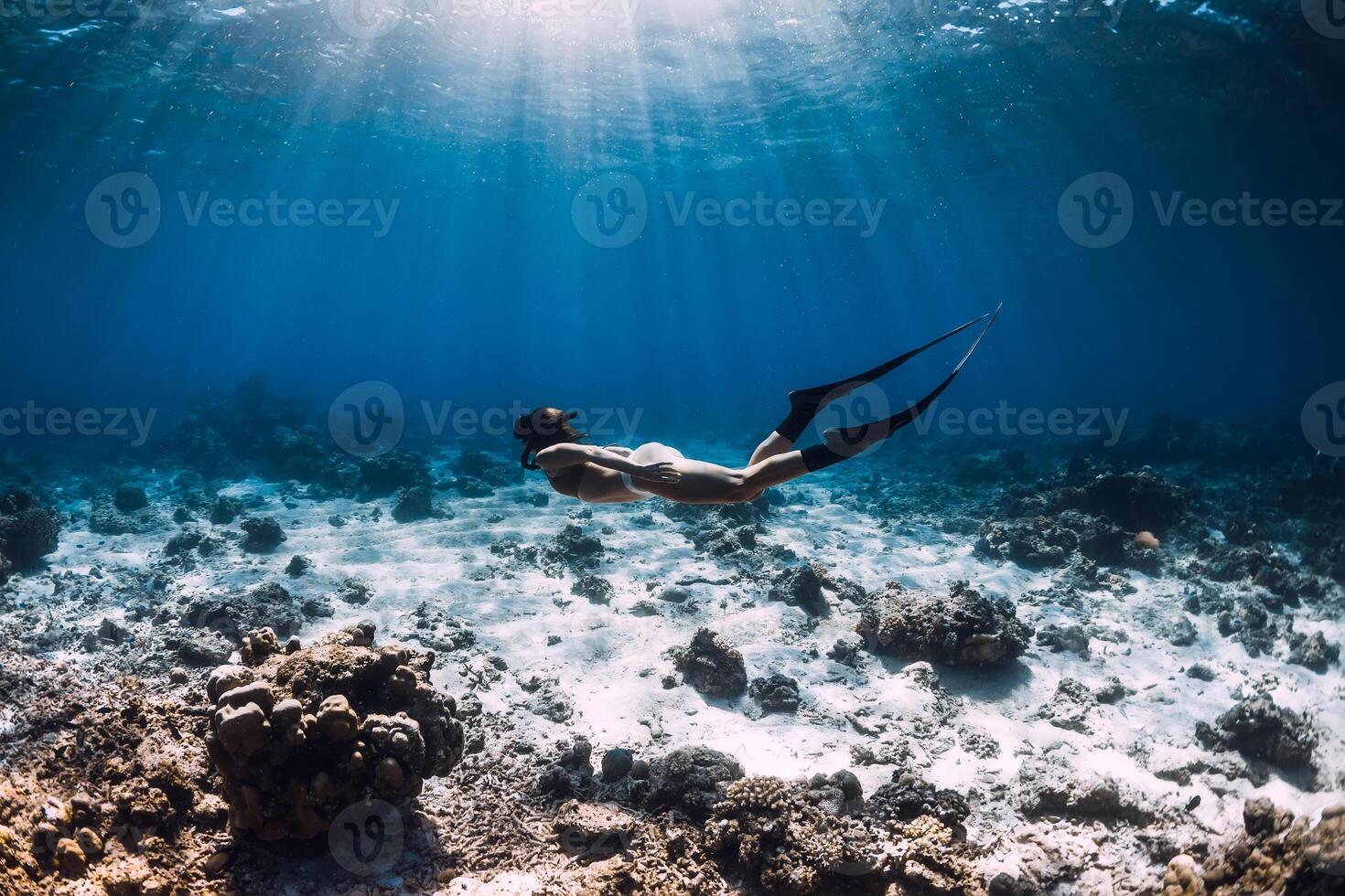 Free diver woman with fins glides over corals in blue sea. photo