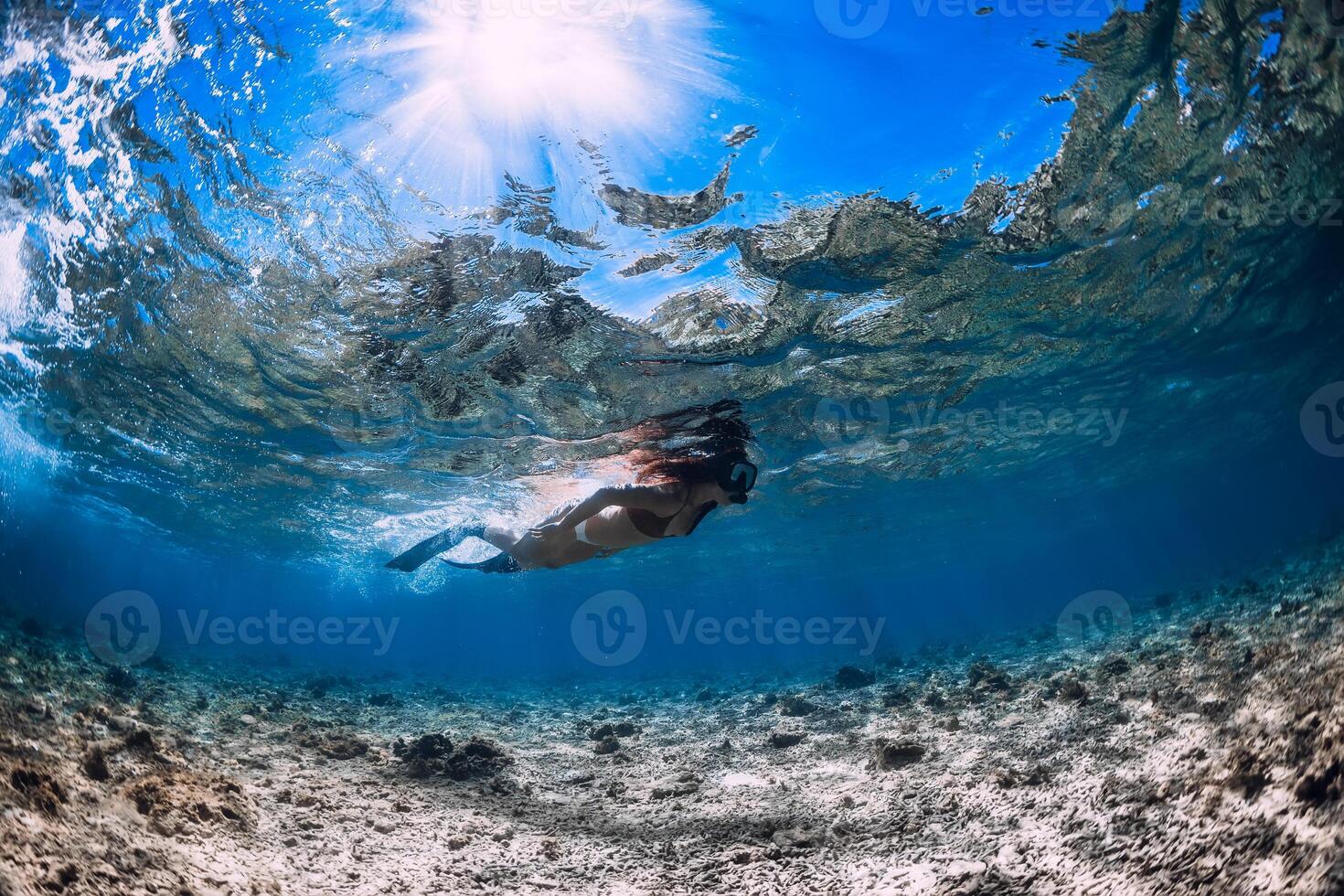 Free diver woman with fins glides over corals in blue sea. photo