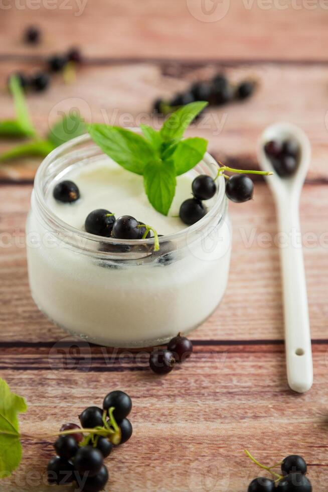 homemade sweet yogurt in a jar with black currants, on a wooden table photo