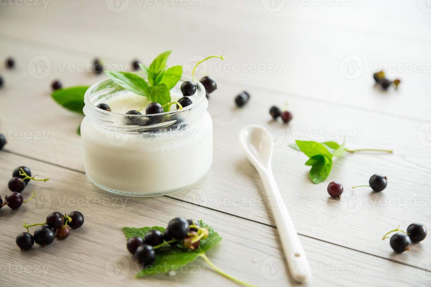 homemade sweet yogurt in a jar with black currants, on a wooden table photo