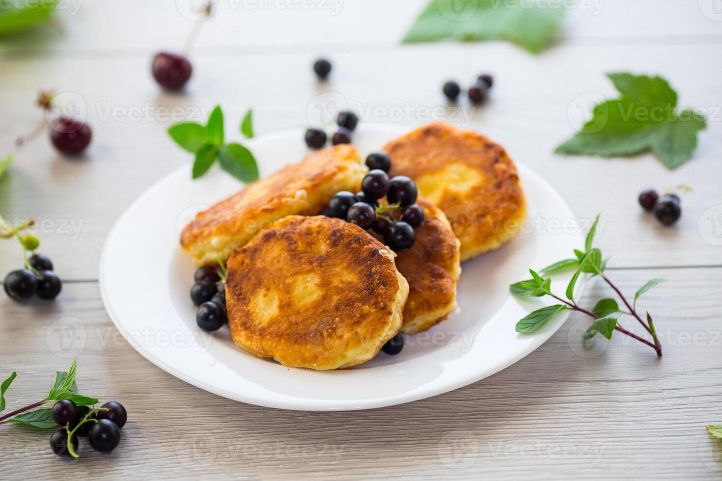 Fried curd cheese pancakes with black currants, on a wooden table photo