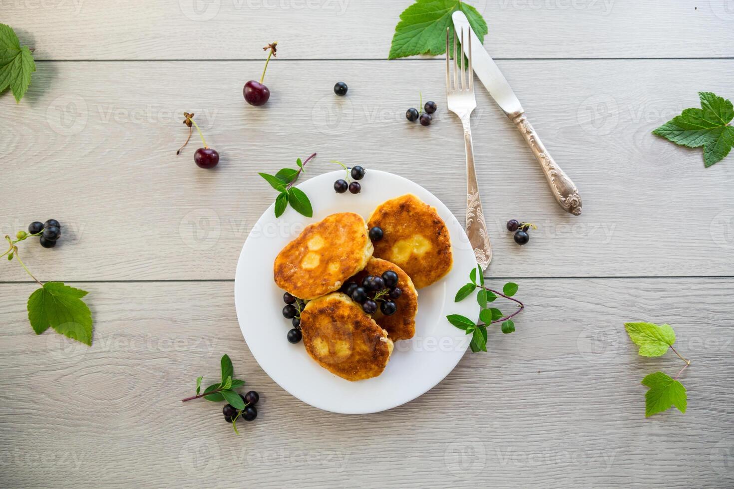 Fried curd cheese pancakes with black currants, on a wooden table photo