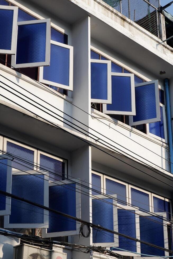 A building facade with multiple blue-tinted windows, some of which are open, creating a visually striking pattern. photo