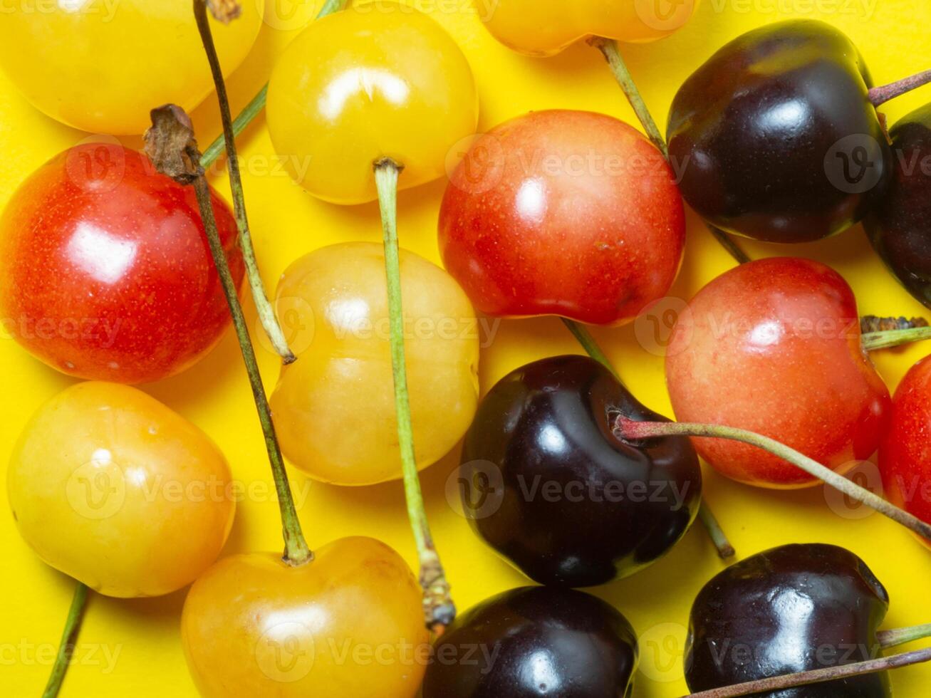 Sweet cherry with a stem on a yellow background. Bright table. Natural berries on the table. Cherries of different varieties. photo