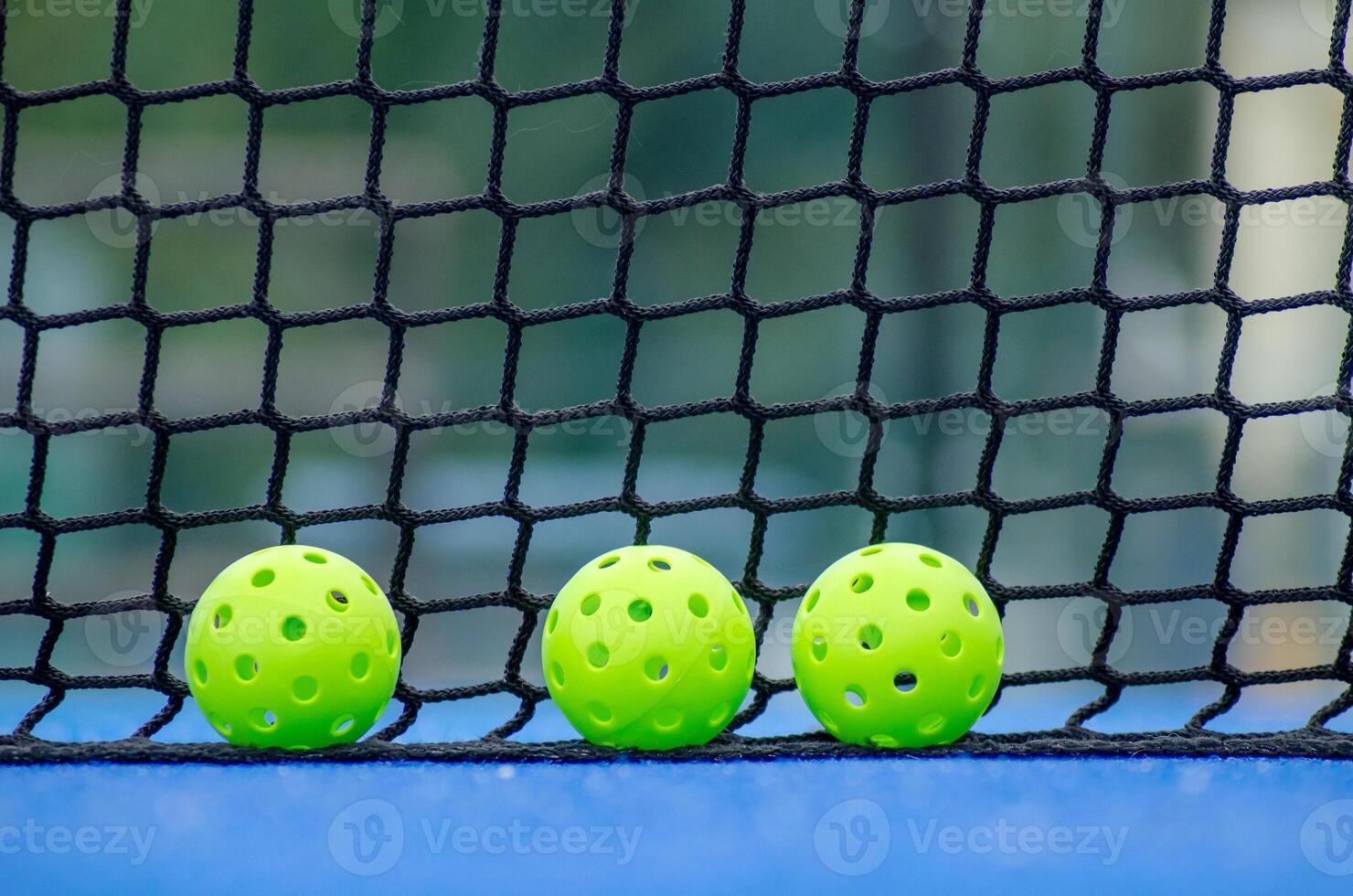 tree green pickleball balls next to the net of a pickleball court photo