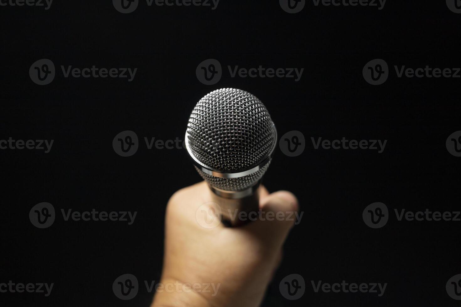 silver microphone Male singer's hand holding microphone on modern singing stage On a black background and hands photo