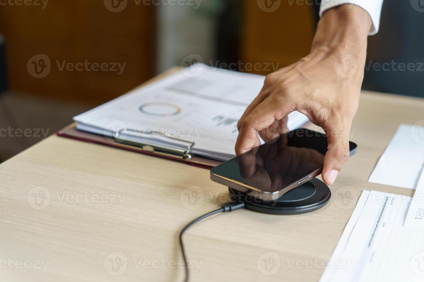 Charging mobile phone battery with wireless charging device in the table. Smartphone charging on a charging pad. Mobile phone near wireless charger Modern lifestyle technology concept photo