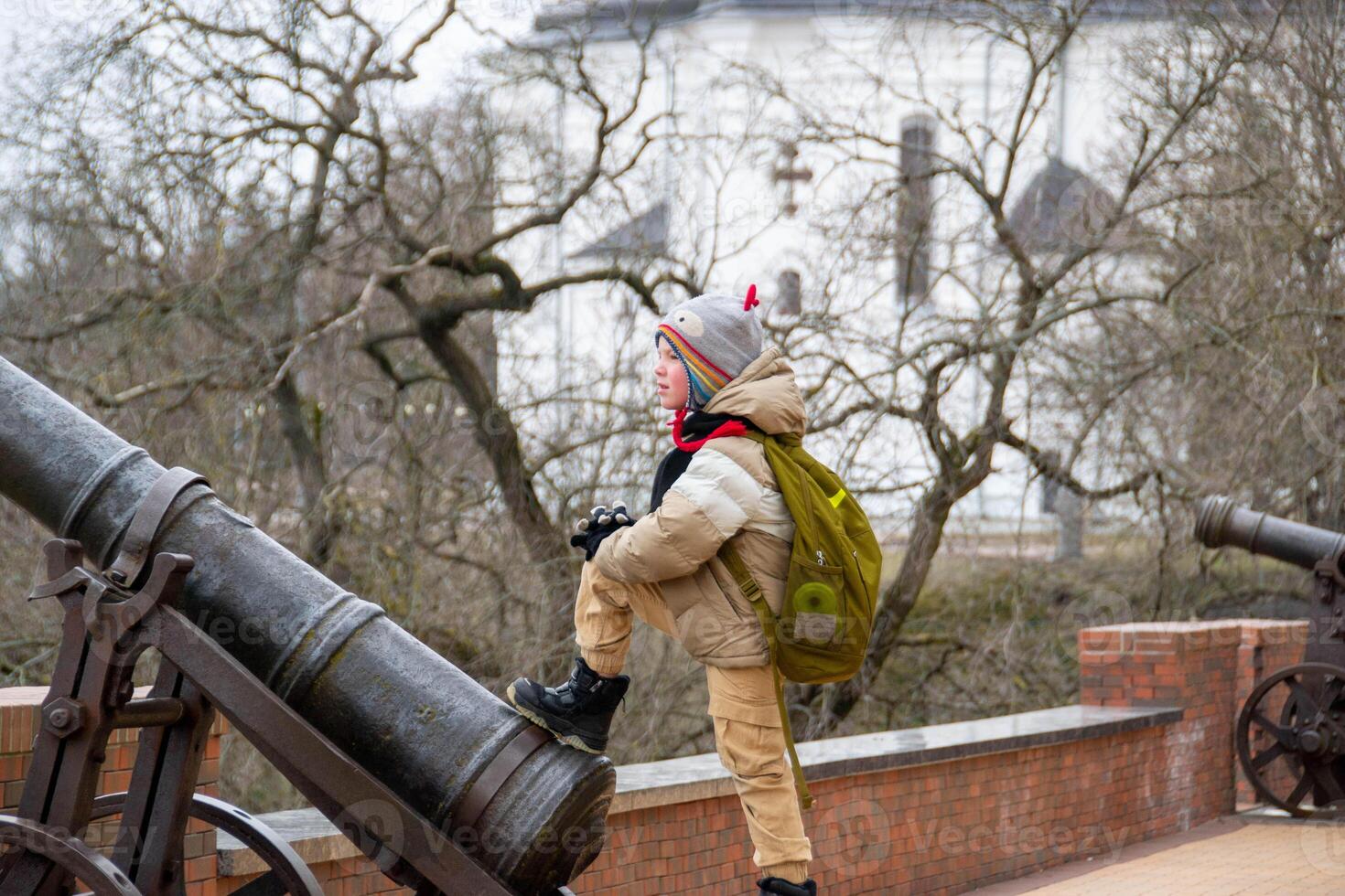 a handsome boy stands against the background of an ancient cannon photo