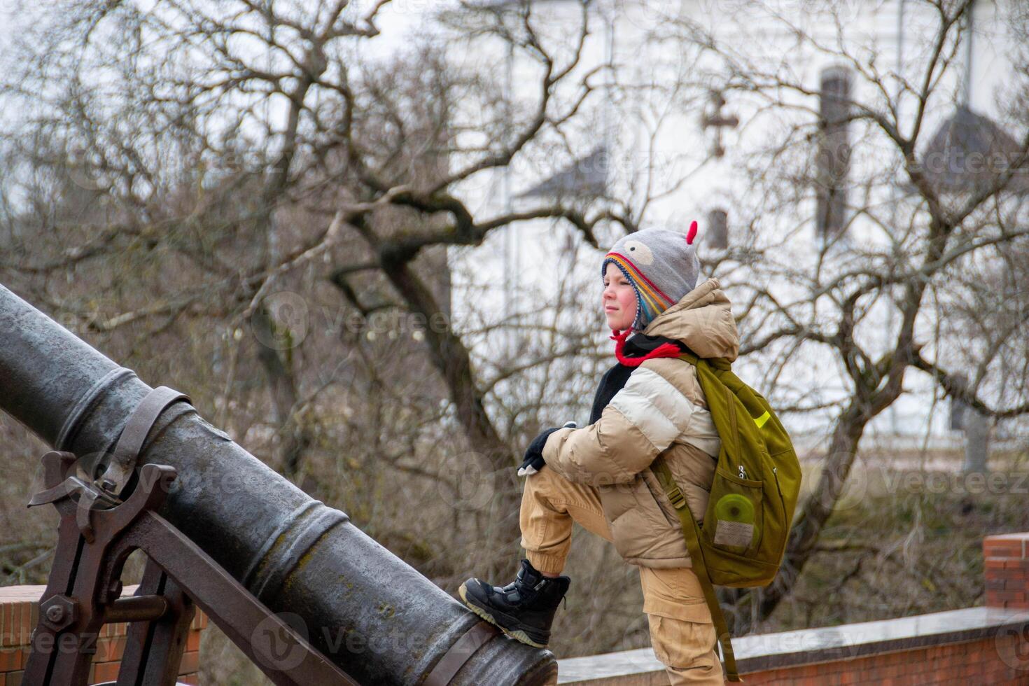 a handsome boy stands against the background of an ancient cannon photo