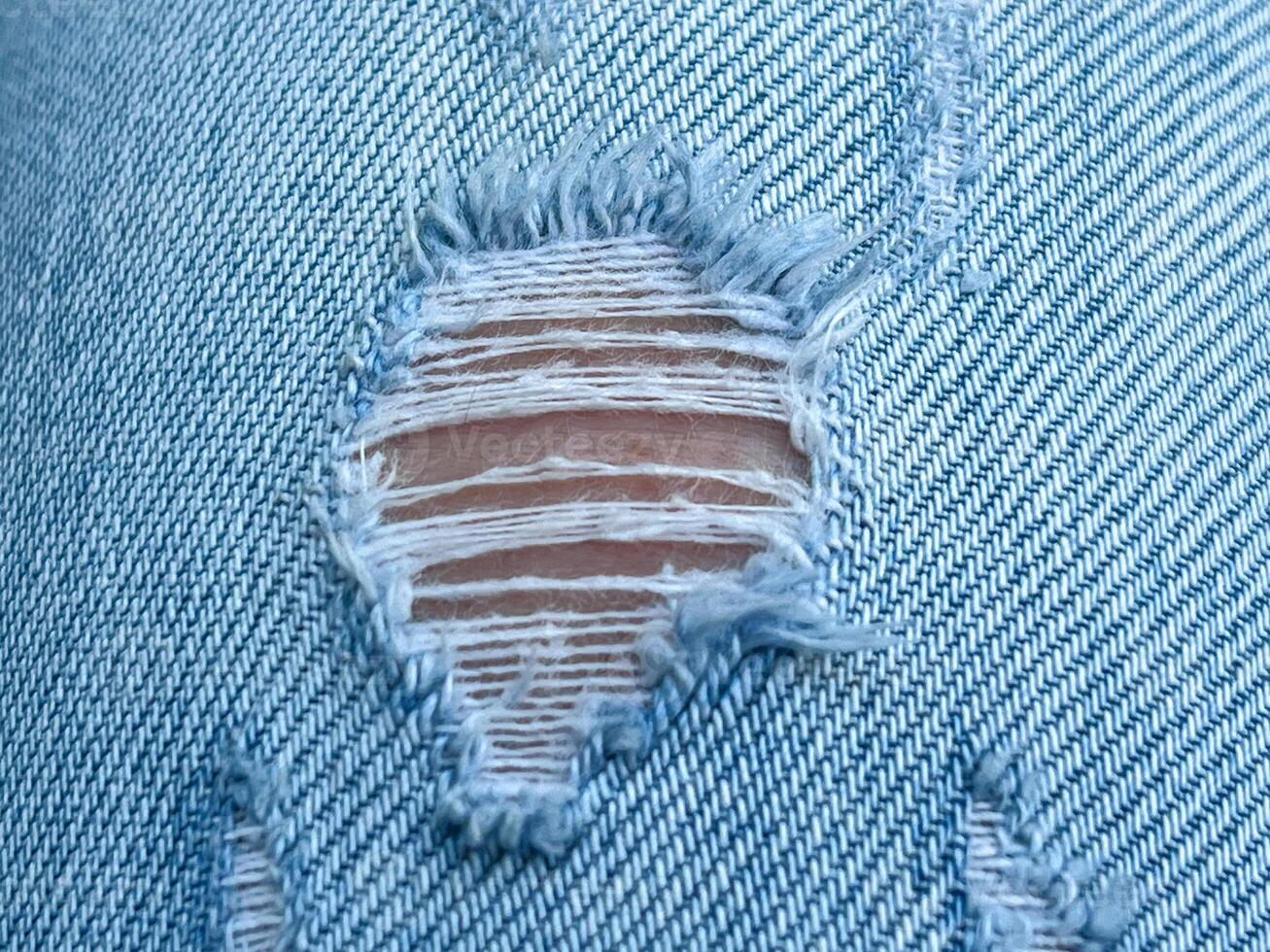 Hole and Threads on Denim Jeans. Ripped Destroyed Torn Blue jeans background. Close up blue jean texture photo