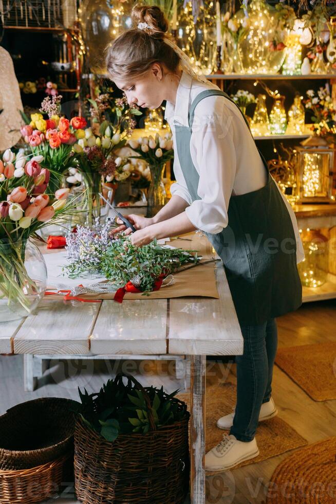 A woman in her florist shop collects bouquets of flowers. The concept of a small business. Bouquets of tulips for the holiday on March 8. photo