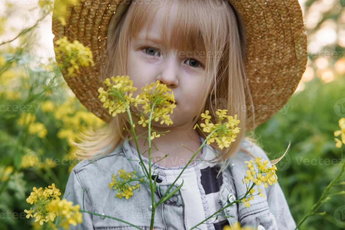 Blonde girl in a field with yellow flowers. A girl in a straw hat is picking flowers in a field. A field with rapeseed. photo
