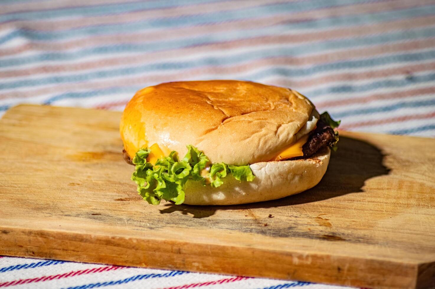 a beef cheese burger filled with meat, tomato sauce, mayonnaise, and lettuce on a cutting board and picnic style cloth that looks delicious and tempting to make hungry stomachs photo