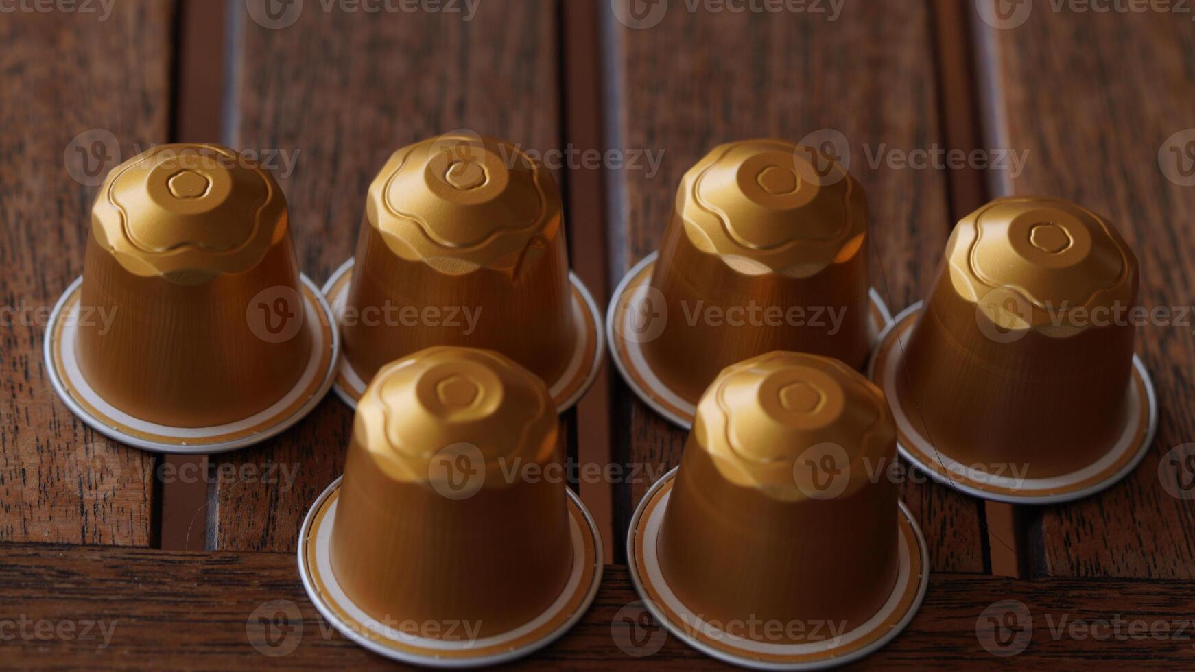 a group of six golden coffee capsules sitting on top of a wooden table photo