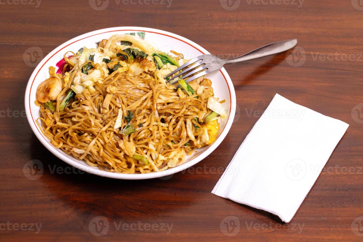 Fried noodle with chicken and vegetables in a white bowl on a wooden table. After edits. photo