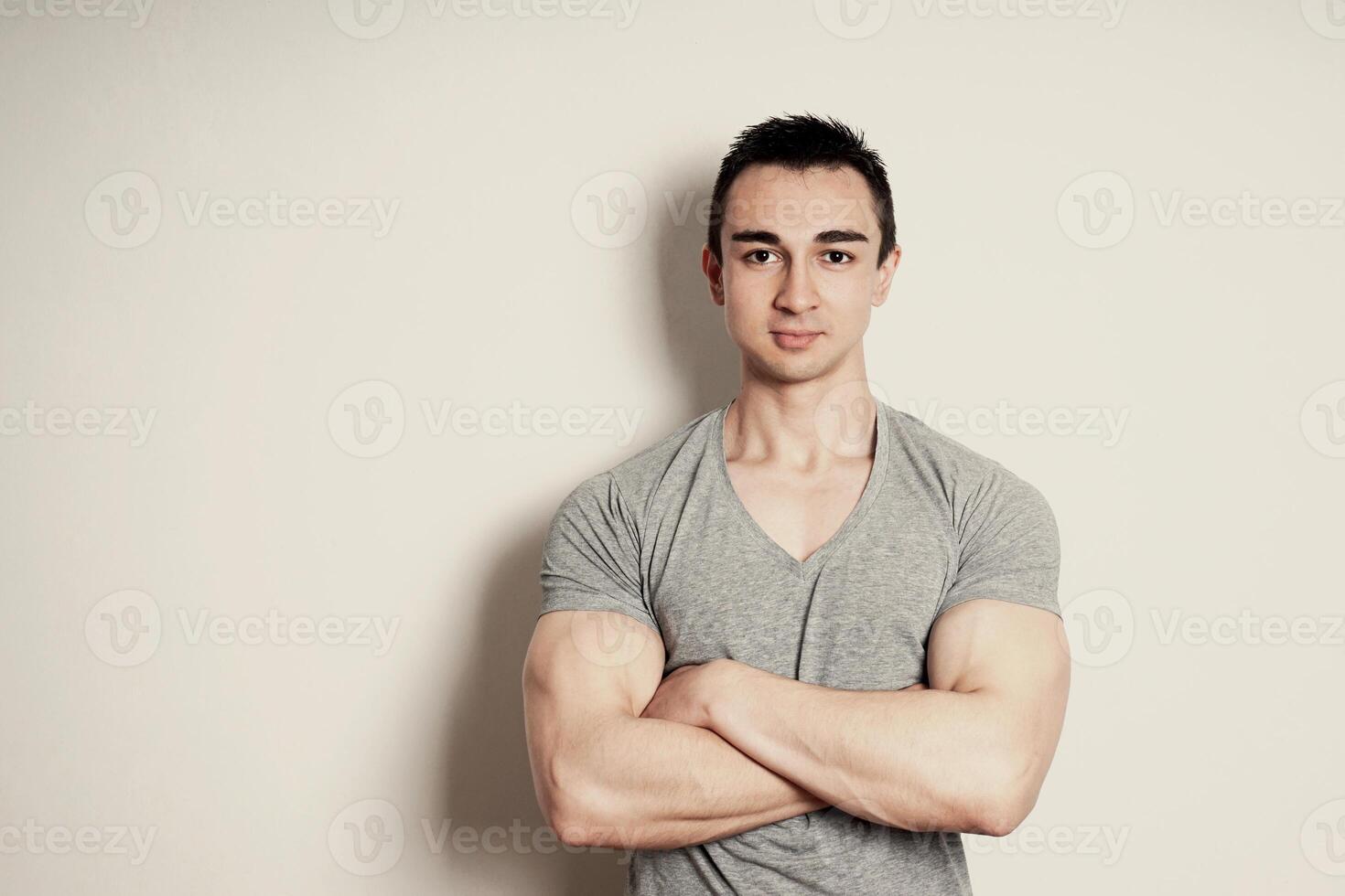 muscular young man with arms crossed standing against wall with copy space photo