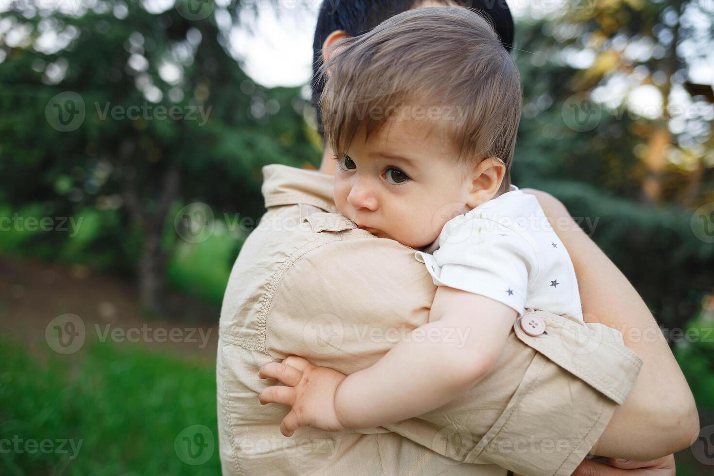 young mom hugs her little son while sitting in the park on the lawn photo