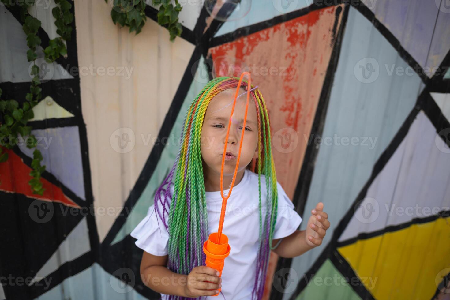 girl with multi-colored afro pigtails inflates soap bubbles against the background of a wall photo