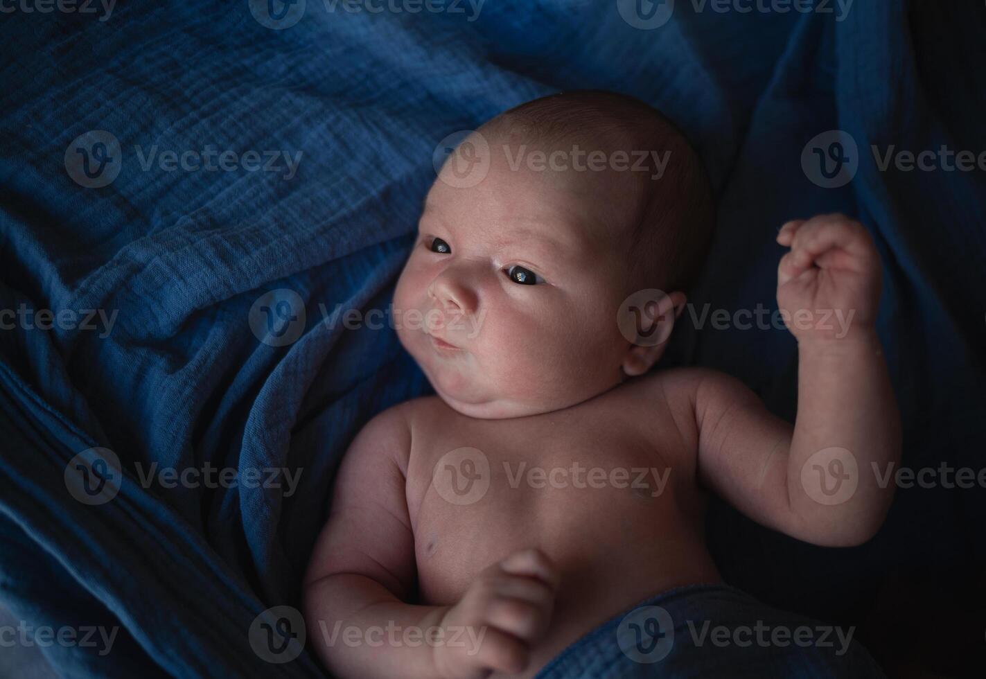 mixed race newborn baby lies wrapped in a blue muslin swaddle photo