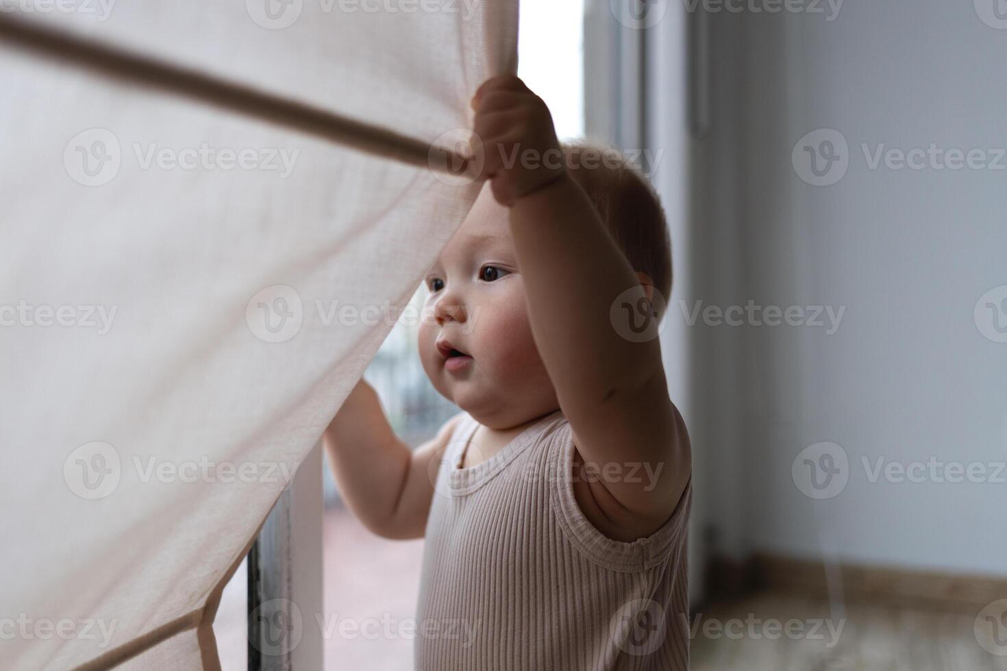 A curious baby pulls the curtain aside, discovering the world beyond the window with wonder photo